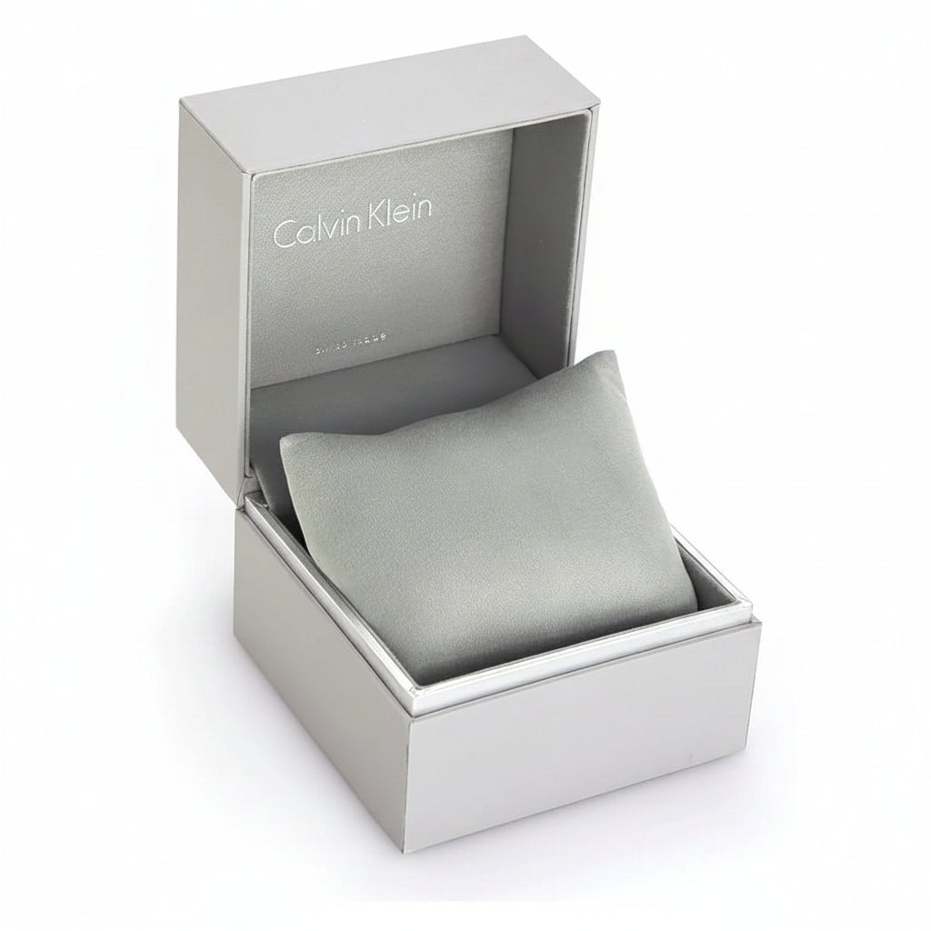 Calvin Klein watch box packaging with the silver-tone outer box open, revealing a light gray cushion inside. The brand name 'Calvin Klein' is printed on the inner lid.